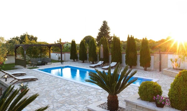 Una piscina con sillones de descanso, una pérgola y diversas plantas.