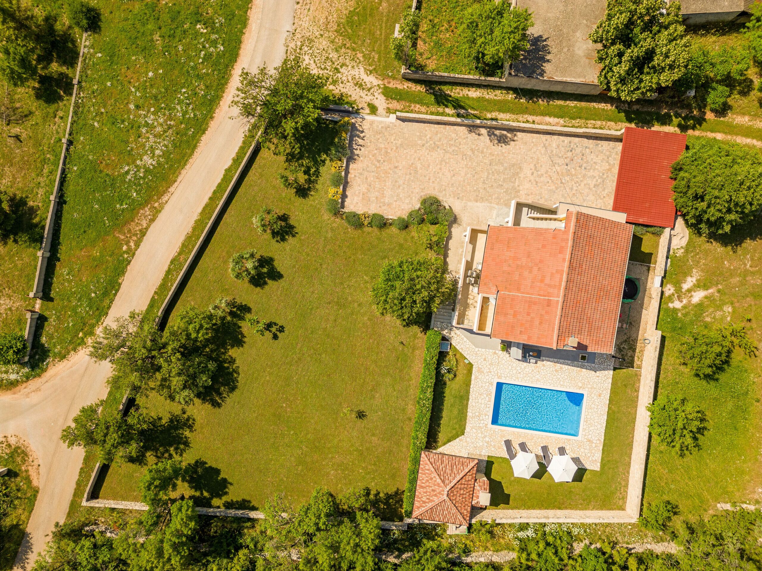 An aerial view of a property with a swimming pool, a red-roofed building, and a well-maintained lawn.
