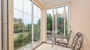 Ein Balkon mit einem Metalltisch und -stuhl, großen Schiebeglastüren und Blick auf Grünflächen sowie ein Gebäude im Hintergrund.