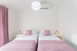 Une chambre double avec deux lits, chacun agrémenté de draps blancs et de touches de rose, un climatiseur blanc et un luminaire suspendu.