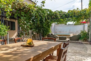 Un espace de restauration en plein air avec une table et des chaises en bois, entouré de verdure et bordé d’un mur blanc.