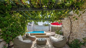 Eine Terrasse mit Korbmöbeln, Steinboden und einem Pool im Hintergrund.