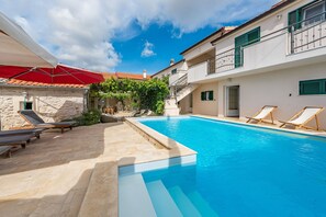 Une piscine avec des chaises longues, un mur en pierre et un parasol rouge.