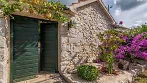 Ein Steinhaus mit einer grünen Tür, ein kleiner Garten mit Bougainvillea und eine Steinmauer.