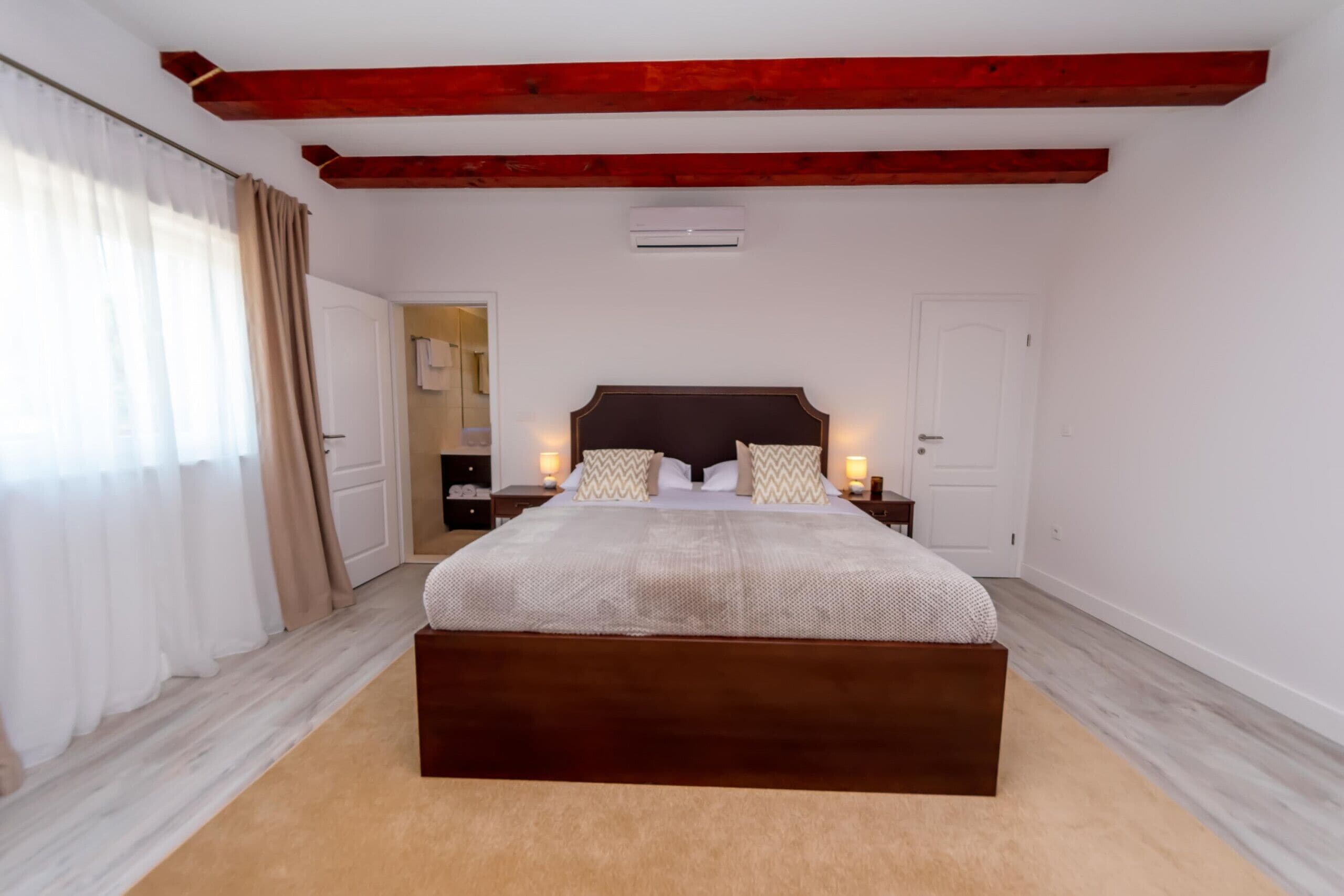 A bedroom with a large bed, wooden beams, a white door, and a white air conditioning unit.