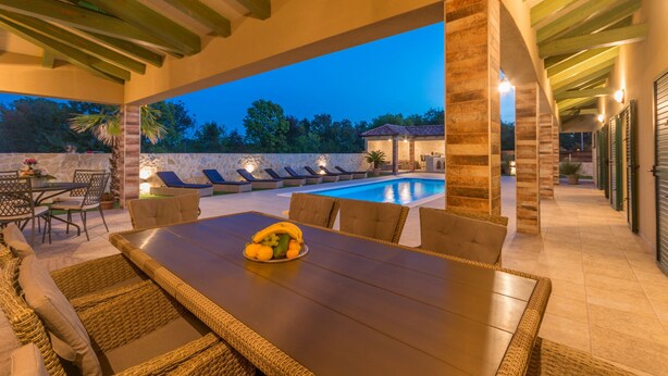 An outdoor dining area with a pool view, stone pillars, and wicker furniture. - Villa Idassa (Policnik)