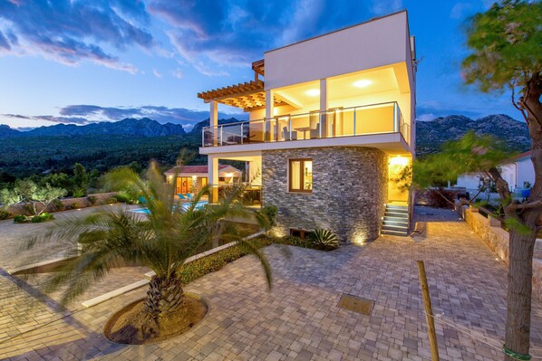 A modern two-story house with a stone facade, a balcony, and a pool.