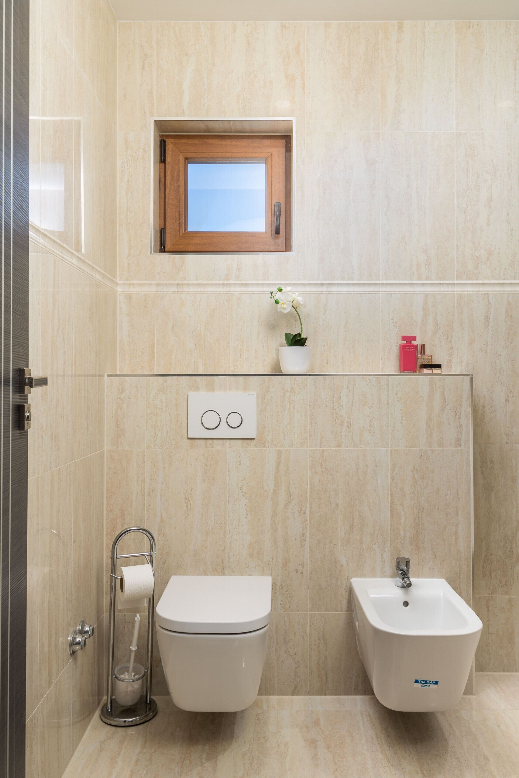 A modern bathroom with a toilet, bidet, and a small window above the sink.