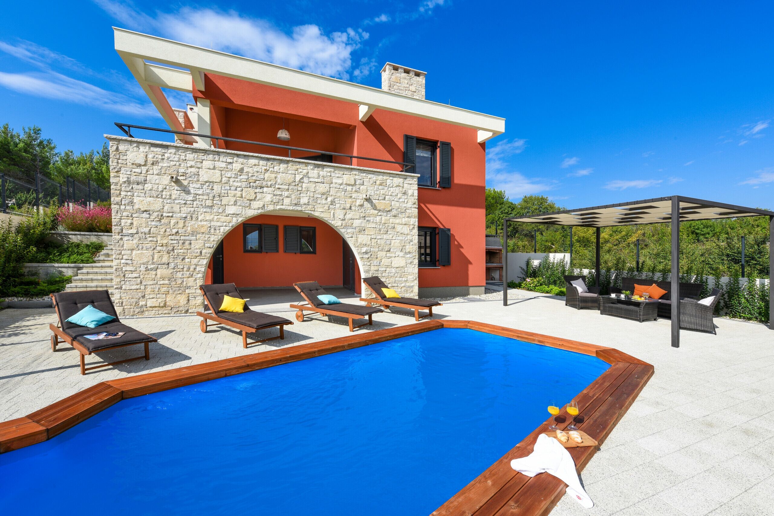 Una casa moderna con piscina, muro de piedra y zona de estar al aire libre.
