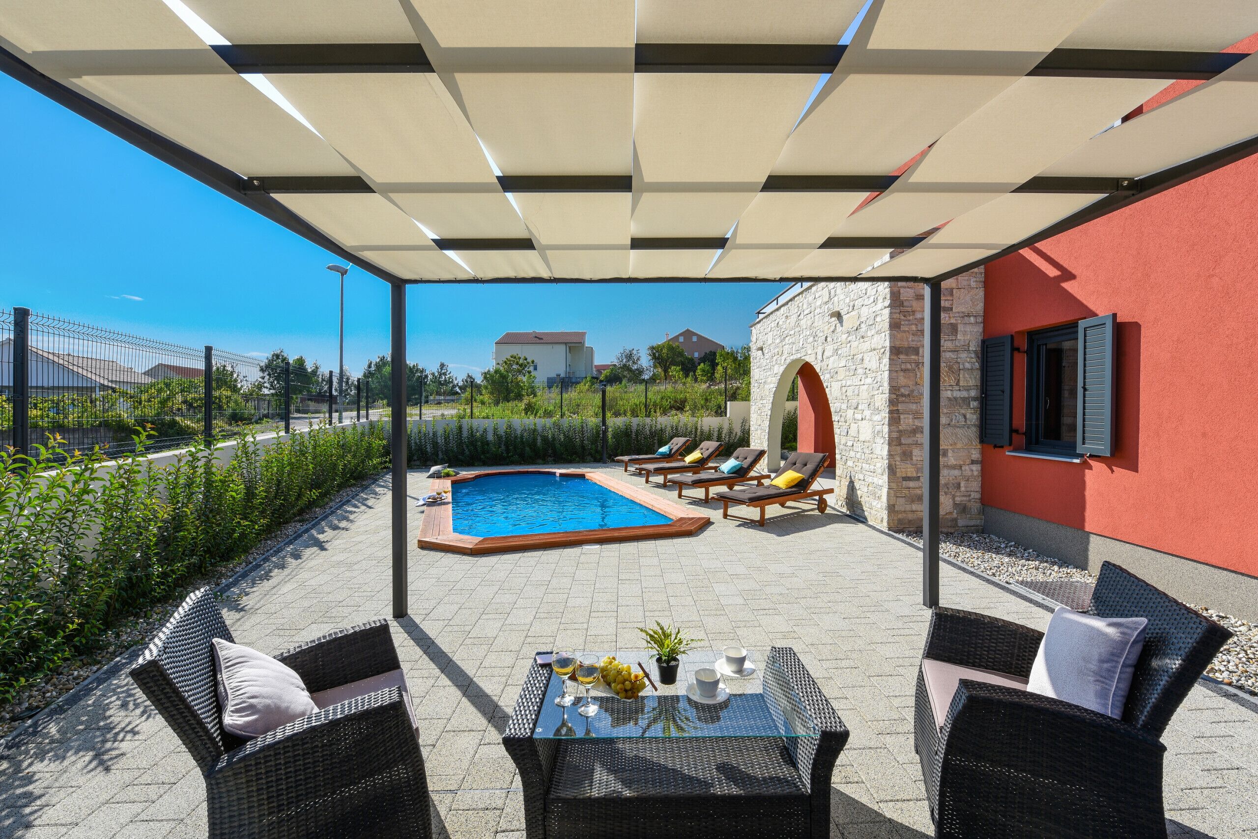 Área externa coberta com piscina, cadeiras de descanso e uma mesa com bebidas e frutas.