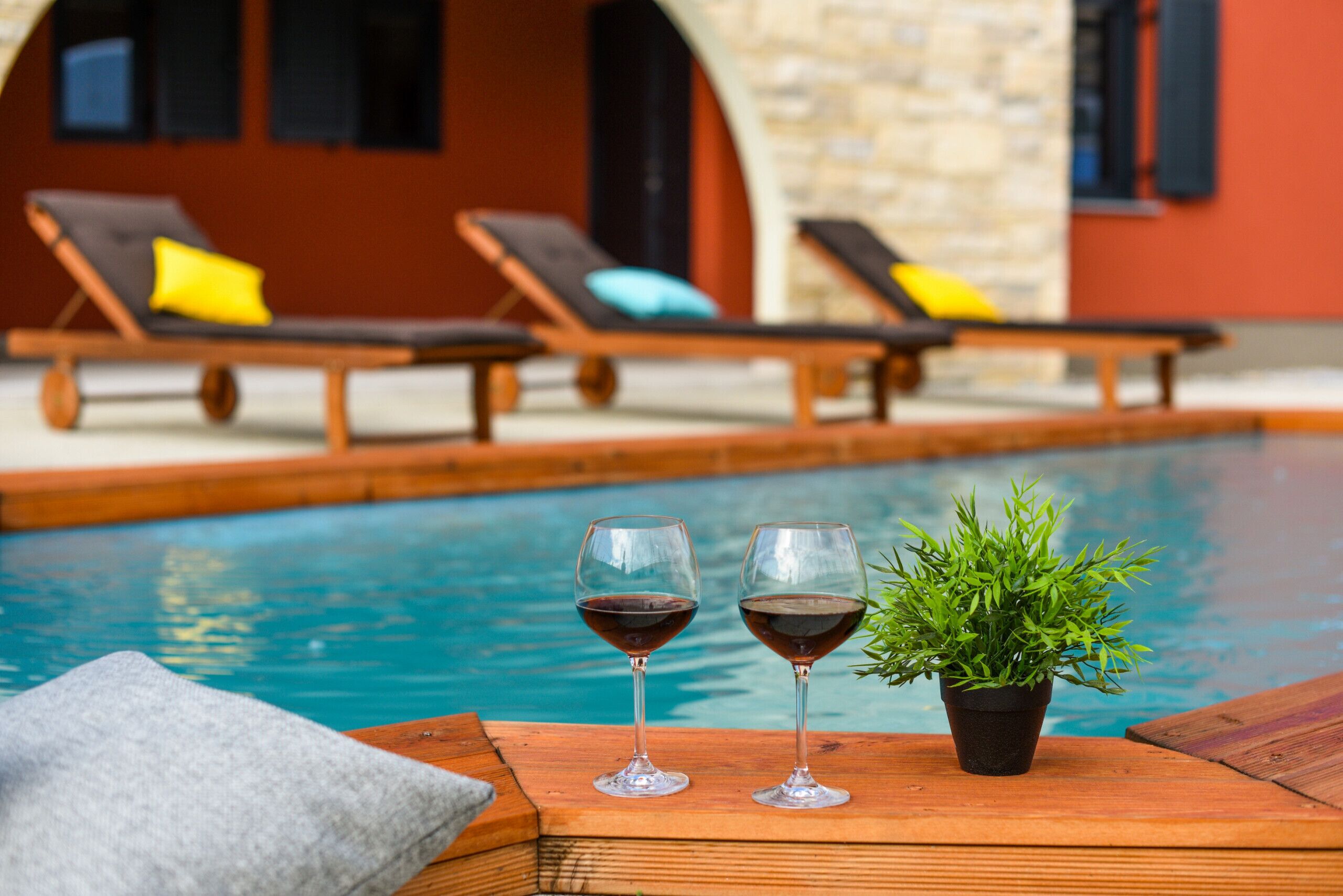 Zona junto a la piscina con sillas de descanso y una pequeña mesa con dos copas de vino y una planta en maceta.