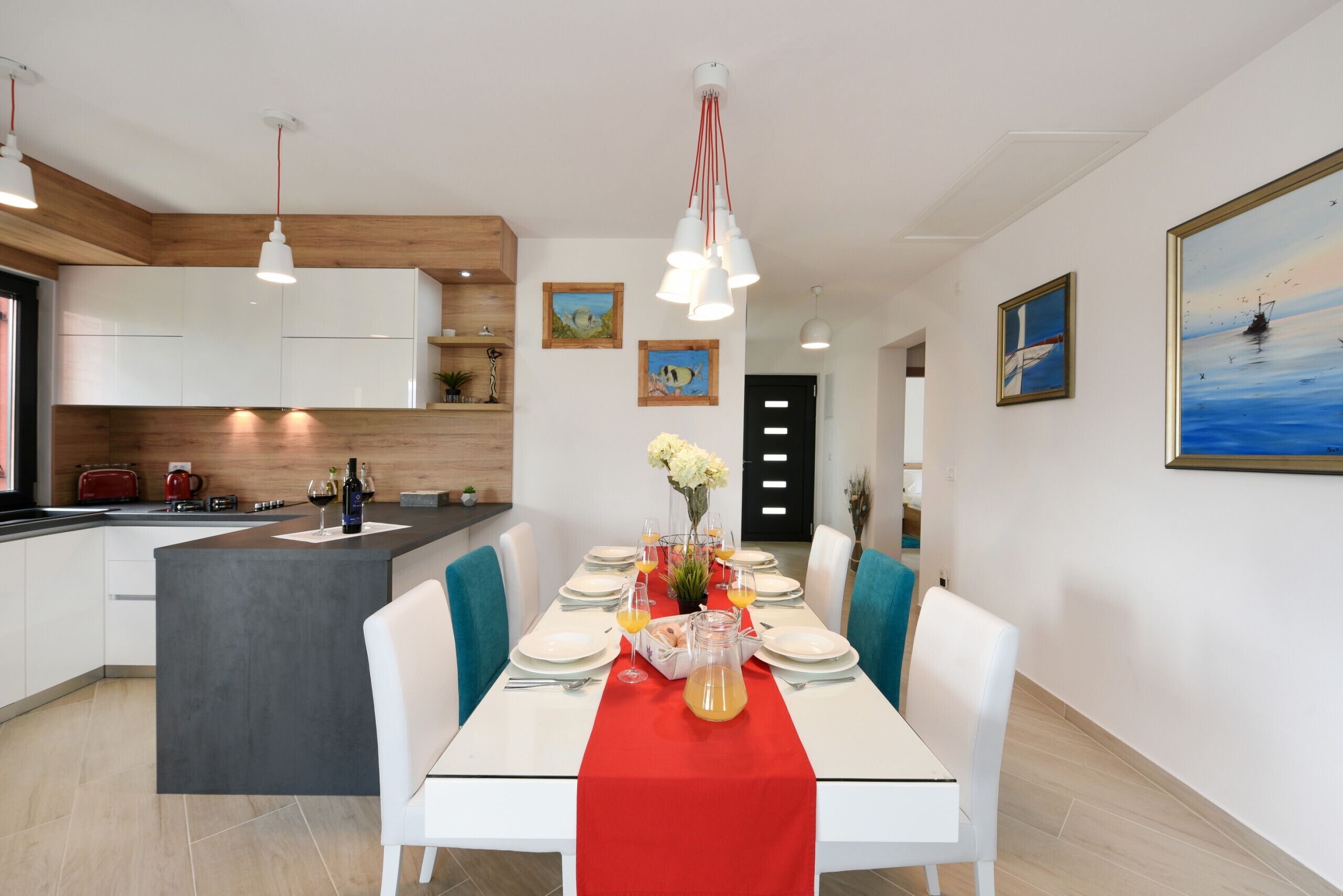 Et moderne køkken med hvide skabe, en central ø og et spiseområde med en rød bordløber.