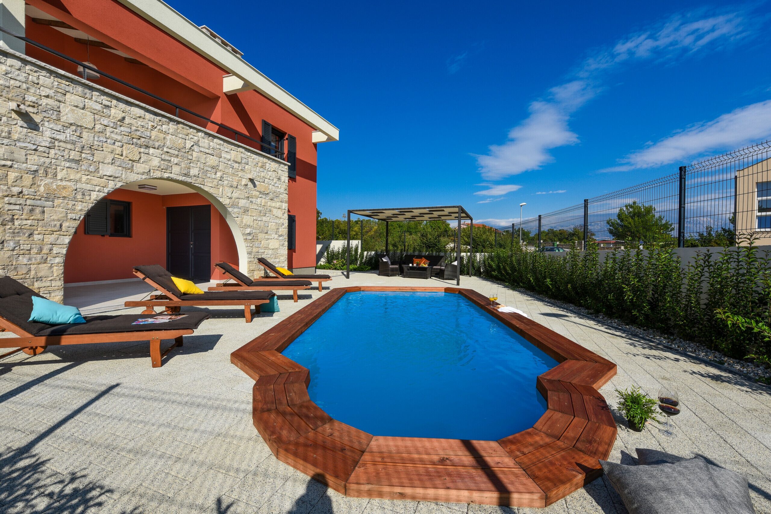 Una piscina con tumbonas de madera y una pared de piedra.