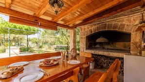 A rustic outdoor dining area with a stone fireplace, wooden benches, and a table set for two. - Villa Krasa (Promina)