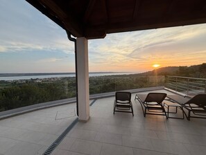 A balcony with a view of a sunset over a landscape, featuring a railing and two chairs. - Villa Lubey (Razanac)