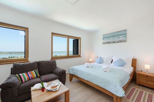 Un dormitorio con cama, sofá, ventana y un cuadro en la pared.