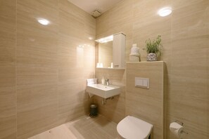 A modern bathroom with a sink, mirror, toilet, and a trash bin.