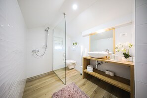 A modern bathroom with a glass shower enclosure, a wooden vanity with a large mirror, and a white sink.