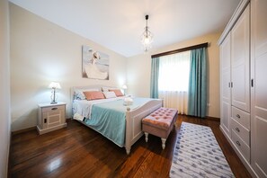 A bedroom with a bed, bedside tables, a bench, a wardrobe, and a chandelier.