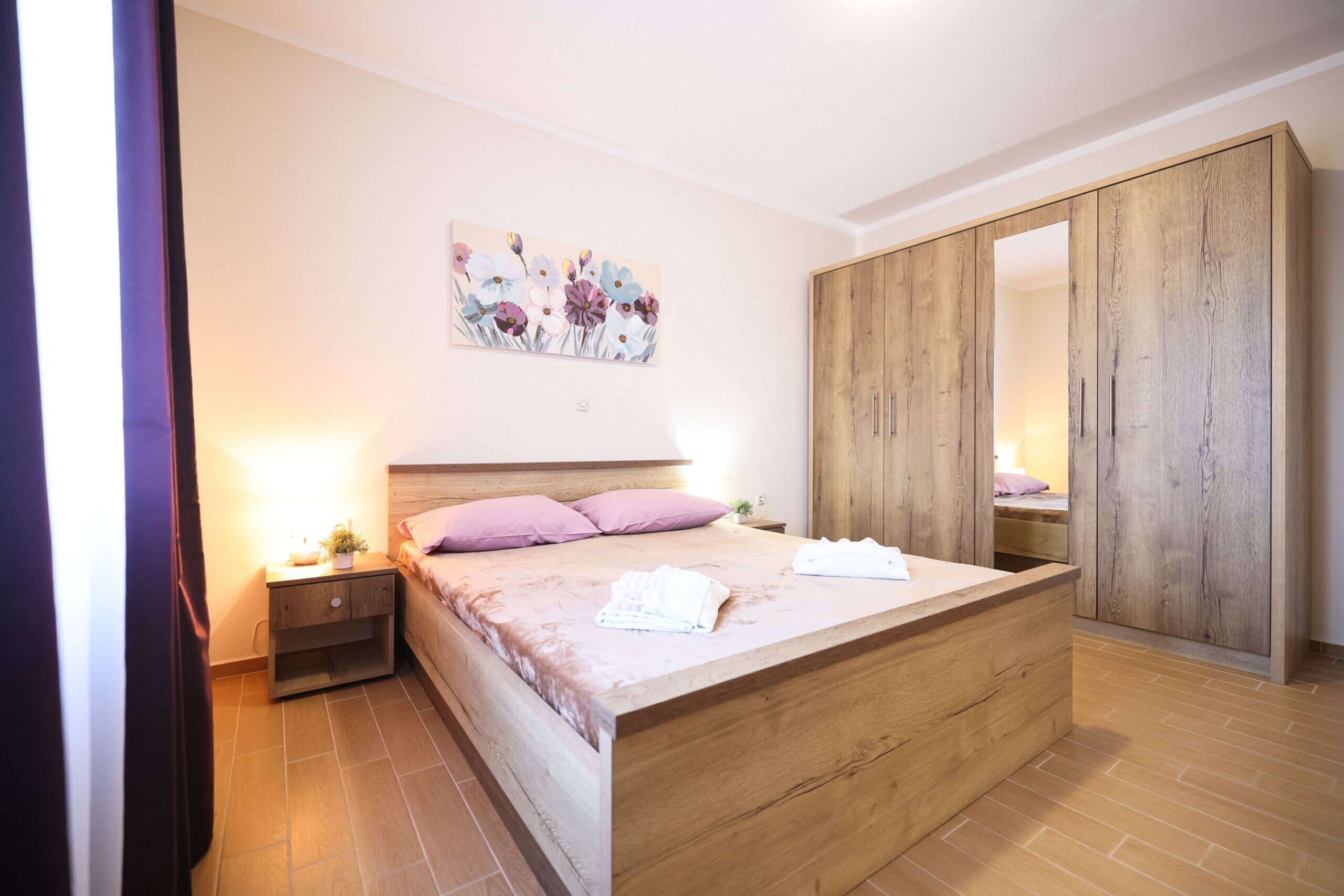 Een slaapkamer met een houten bed, nachtkastje, kledingkast en een bloemendecoratie aan de muur.