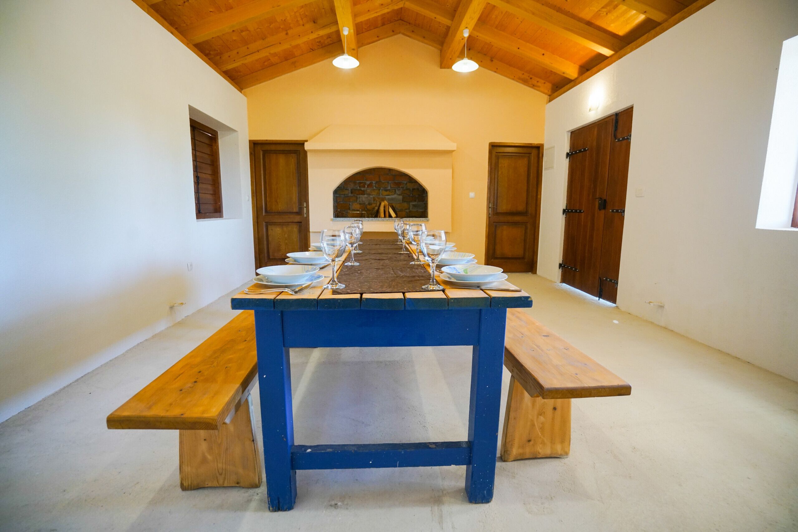 Una larga mesa de comedor con bancos, una chimenea de piedra y puertas de madera.