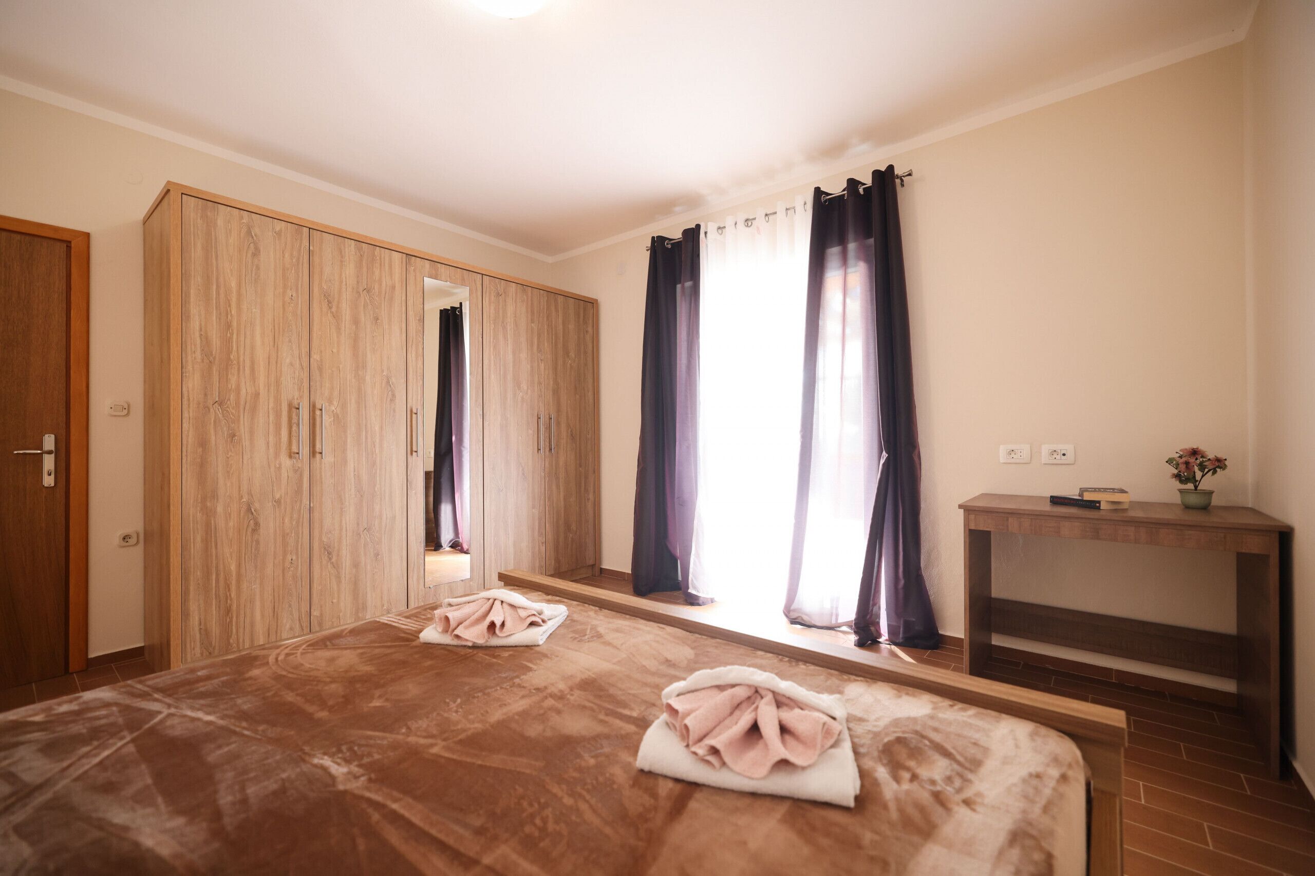 A bedroom with a large bed, wooden wardrobe, and a small table with a vase.