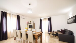 Una sala de estar moderna con comedor, que incluye una mesa de comedor de madera, sillas blancas, un sofá gris y una pequeña mesita auxiliar.