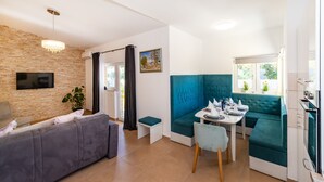 A modern living space with a stone wall, a flat-screen TV, a sofa, a dining table set, and a kitchen area. - Villa Didov Dvor (Posedarje)