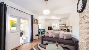 A modern living room with a sofa, a glass coffee table, and a view of the kitchen. - Villa Didov Dvor (Posedarje)