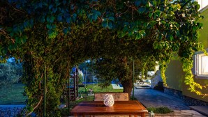 An outdoor patio with a wooden table and chairs, surrounded by lush greenery and a stone pathway. - Villa Didov Dvor (Posedarje)