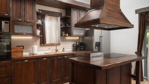 A modern kitchen with dark wooden cabinets, a central island, and a stainless steel range hood. - Villa Quince (Policnik)