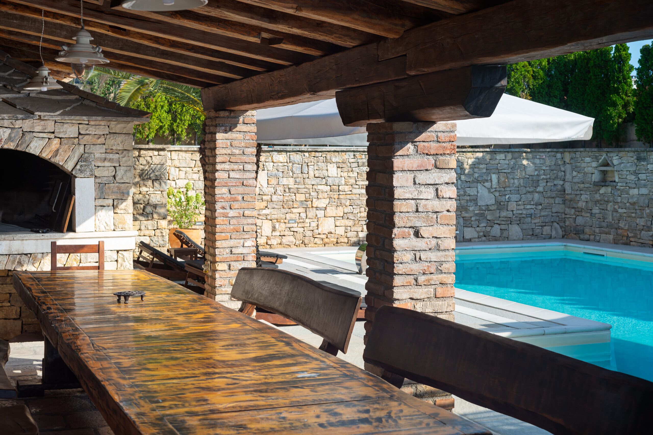 An outdoor patio with a stone fireplace, a pool, and a wooden table.