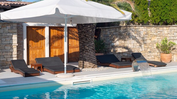 A poolside area with lounge chairs, a stone wall, and a wooden door. - Villa Quince (Policnik)