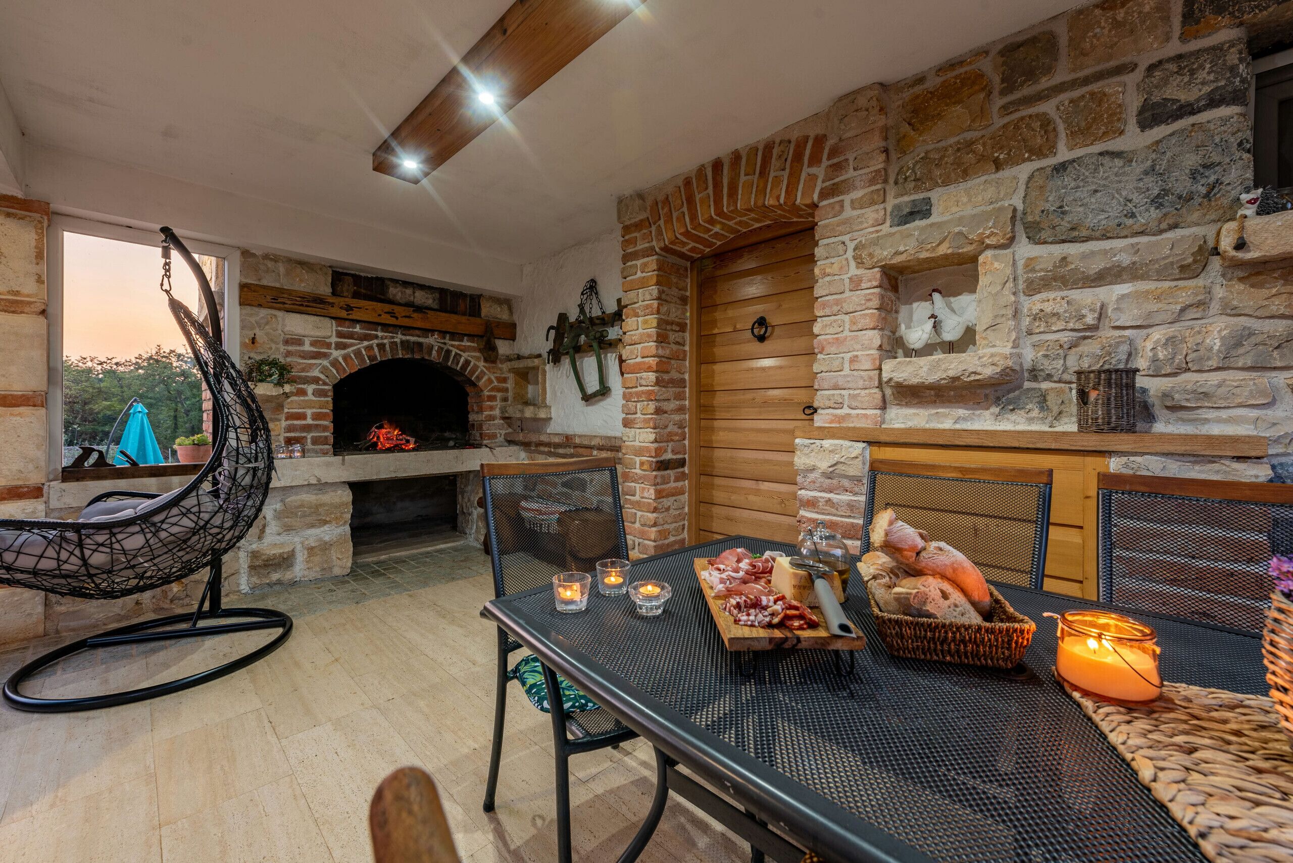 A cozy outdoor seating area with a stone fireplace, wicker furniture, and a table set with food and candles.