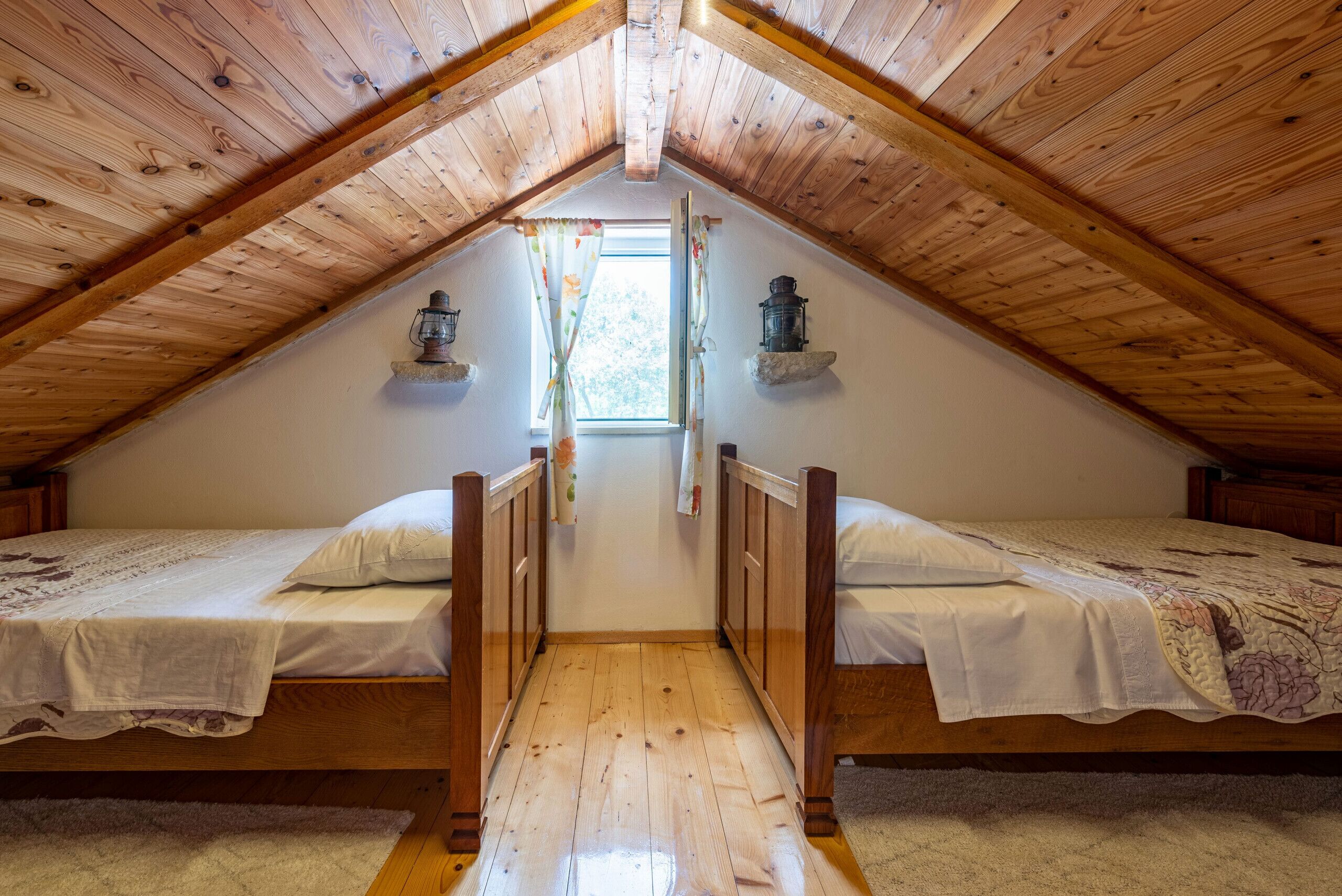 A bedroom with two wooden beds, a wooden ceiling, and a window with curtains.