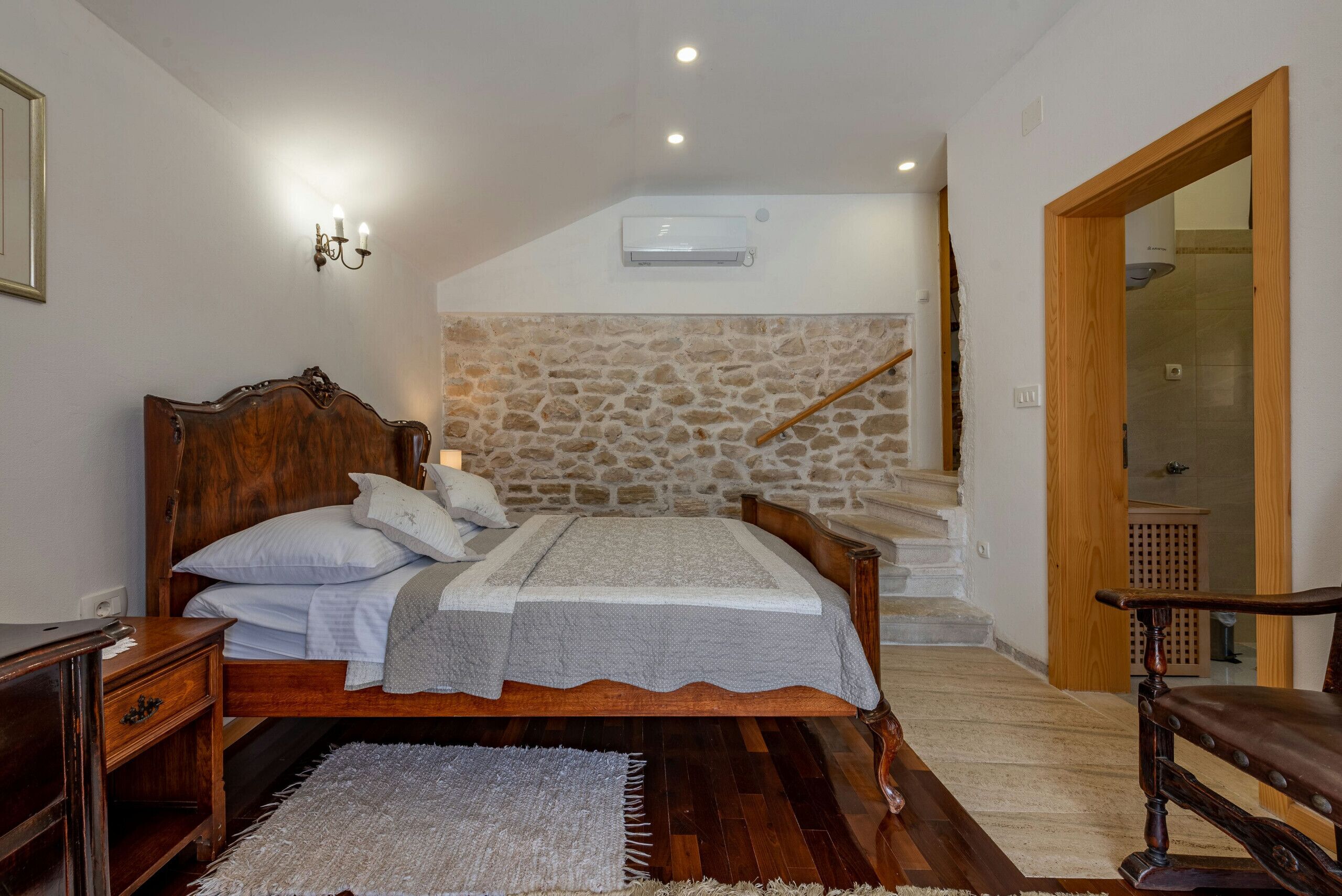 A bedroom with a wooden bed, stone wall, and a staircase leading to an upper level.