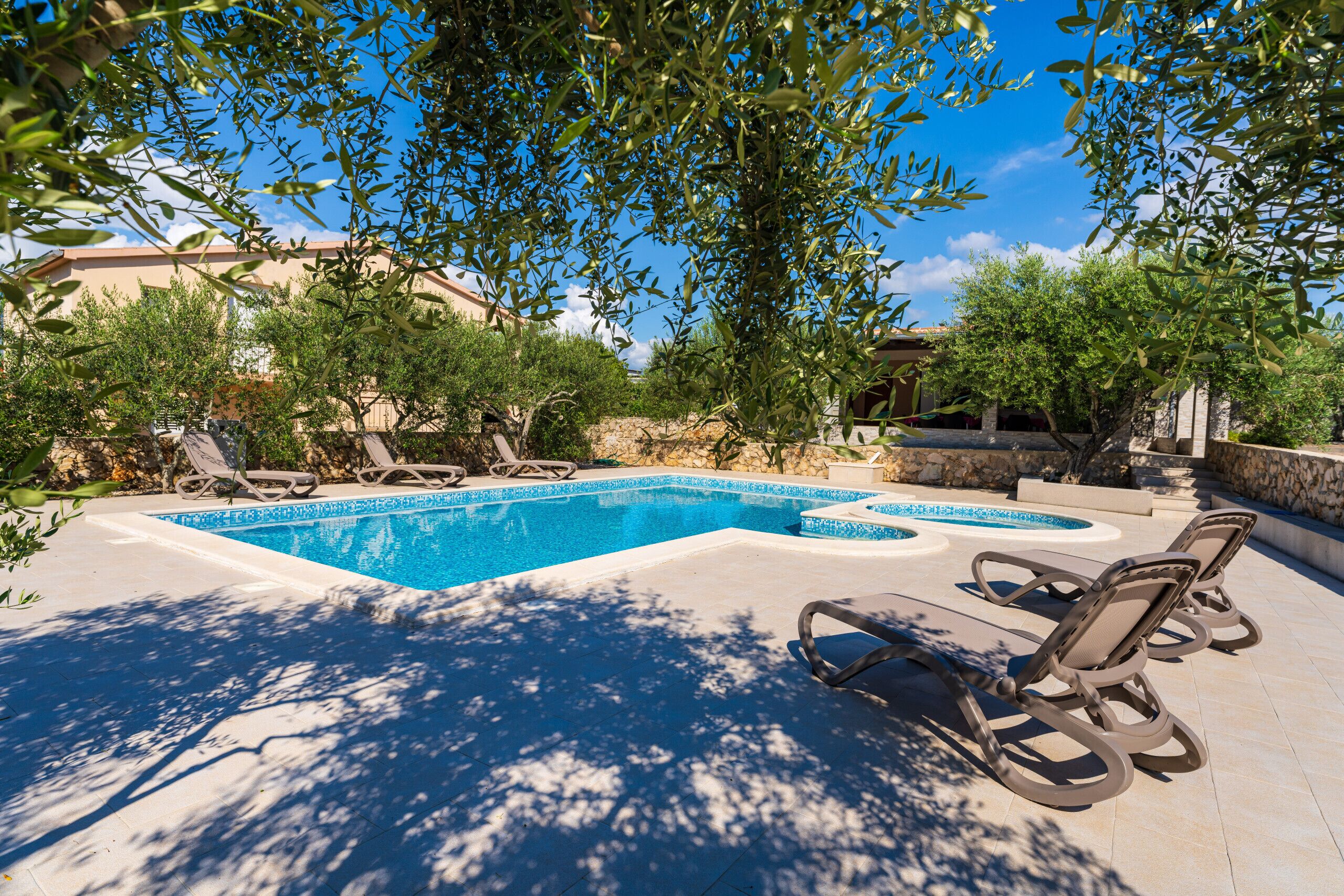 A swimming pool with lounge chairs, surrounded by trees and a stone wall.
