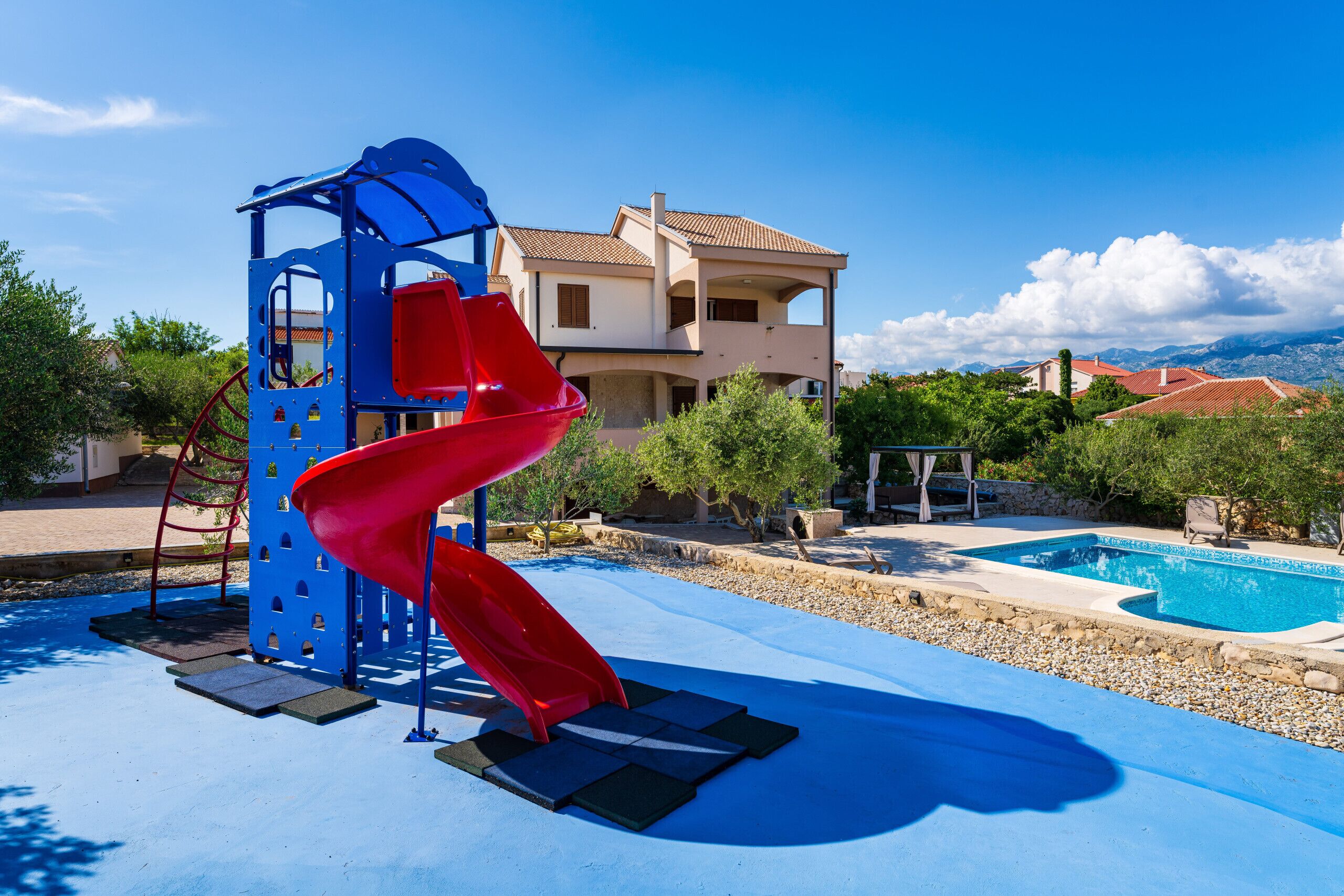 A playground with a red slide, a pool, and a building in the background.