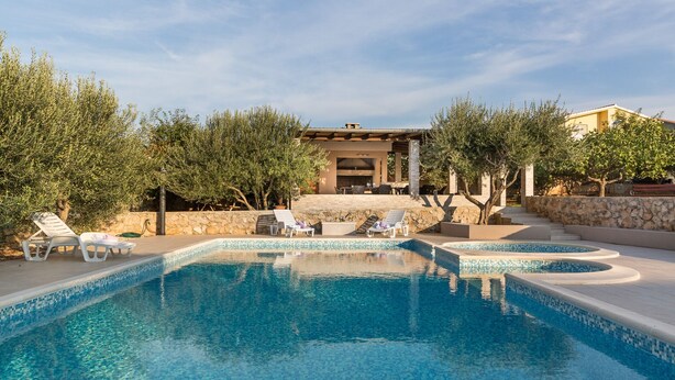 Piscina con sillas de descanso, pared de piedra y zona exterior cubierta con una parrilla.