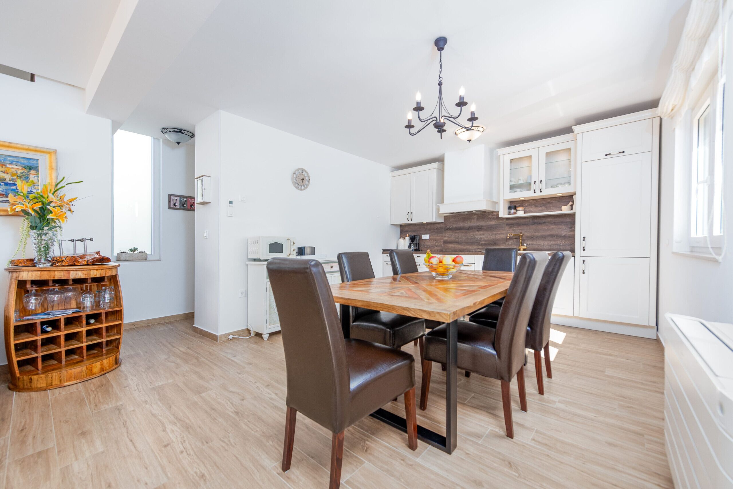 Una cocina moderna con armarios blancos, una mesa de comedor de madera con sillas y una lámpara de araña.
