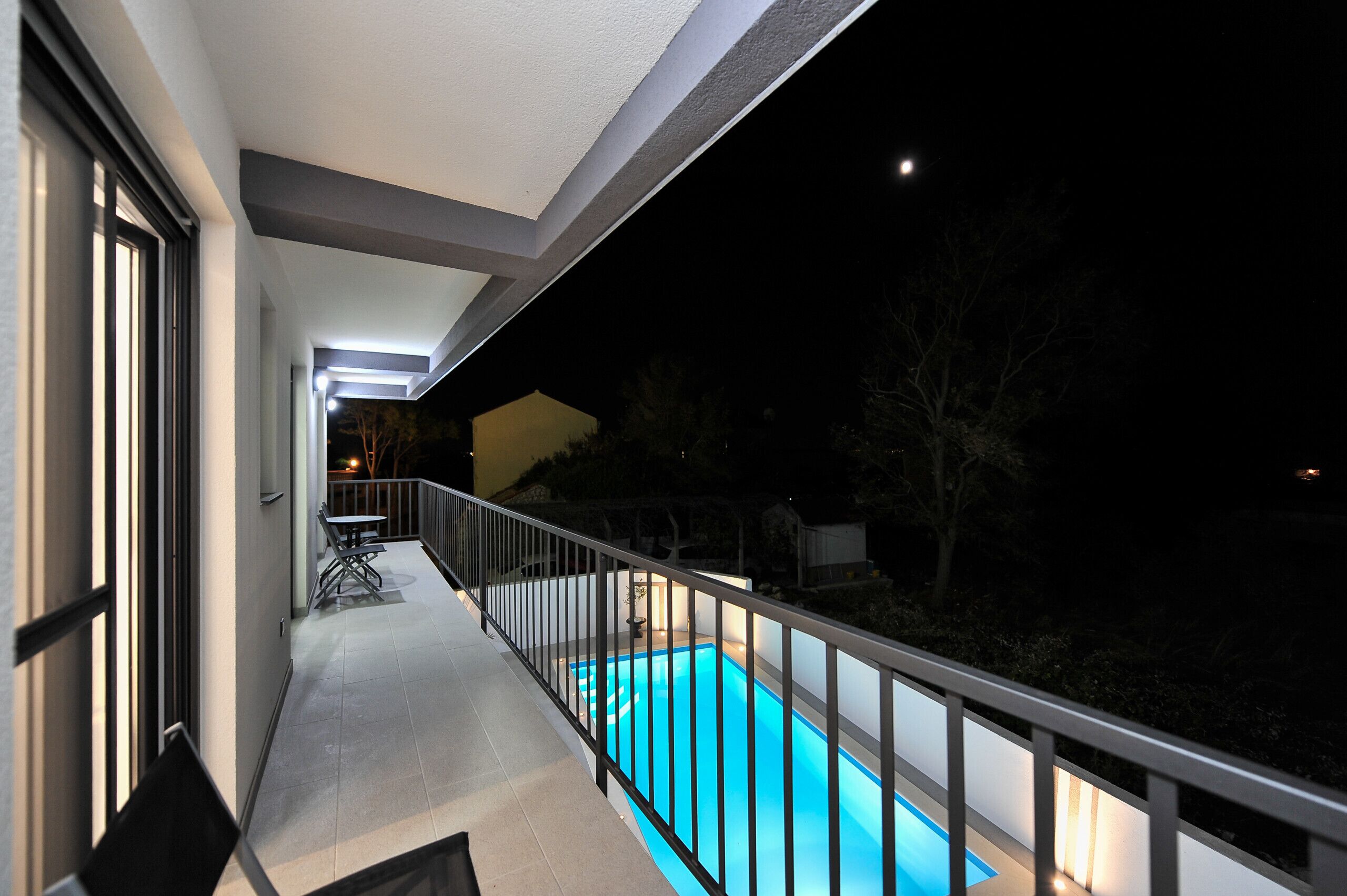 Un balcón con piscina, una mesa y sillas, y vista al cielo nocturno.