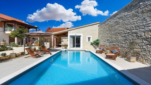 Una piscina con sillas de descanso, un muro de piedra y un edificio con techo de tejas.