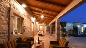 Un rincón exterior acogedor con paredes de piedra y vigas de madera, que incluye una mesa con sillas y una botella.