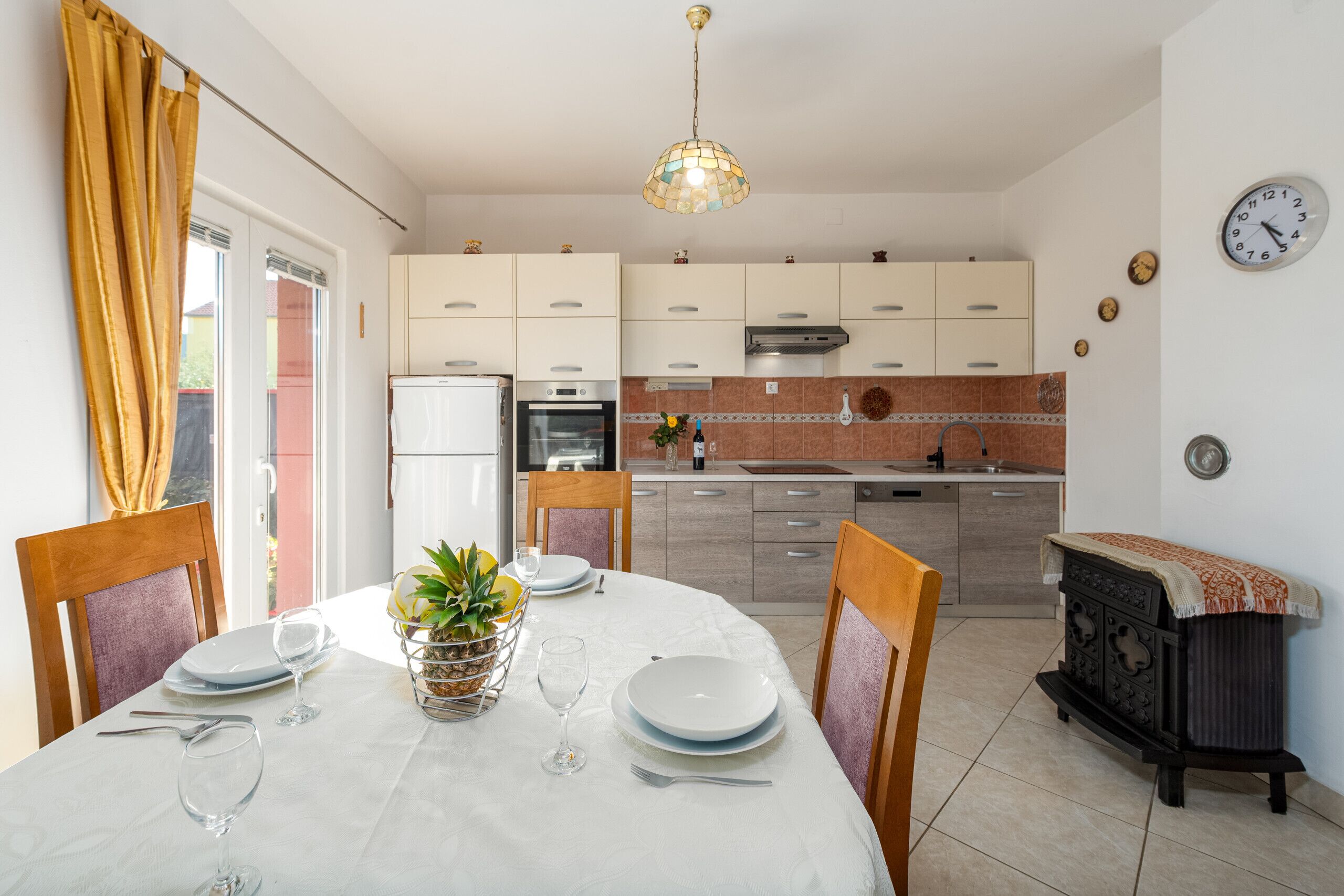 A modern kitchen with white cabinets, a stove, and a sink. There is a dining table with chairs and a chandelier.