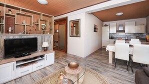 Una sala de estar moderna con un televisor de pantalla plana, estanterías de madera y un comedor con mesa y sillas.