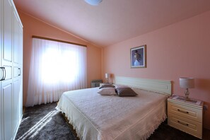 Ein Schlafzimmer mit einem großen Bett, einem Nachttisch, einer Kommode und einem Fenster mit durchsichtigen Vorhängen.