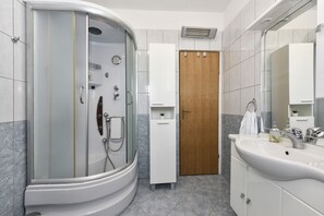 Een moderne badkamer met een inloopdouche, een houten deur, een wit kastje en een grote spiegel.