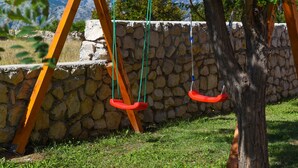 A swing set with two swings, a stone wall, and a grassy area. - Villa Nea (Posedarje)