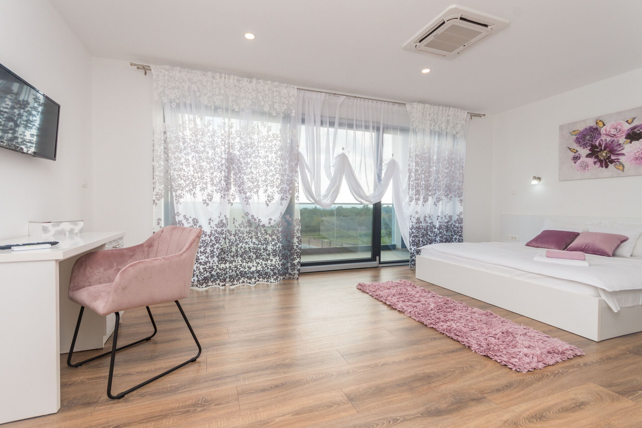Une chambre à coucher comprenant un lit, un bureau, une chaise et une fenêtre ornée de rideaux légers.