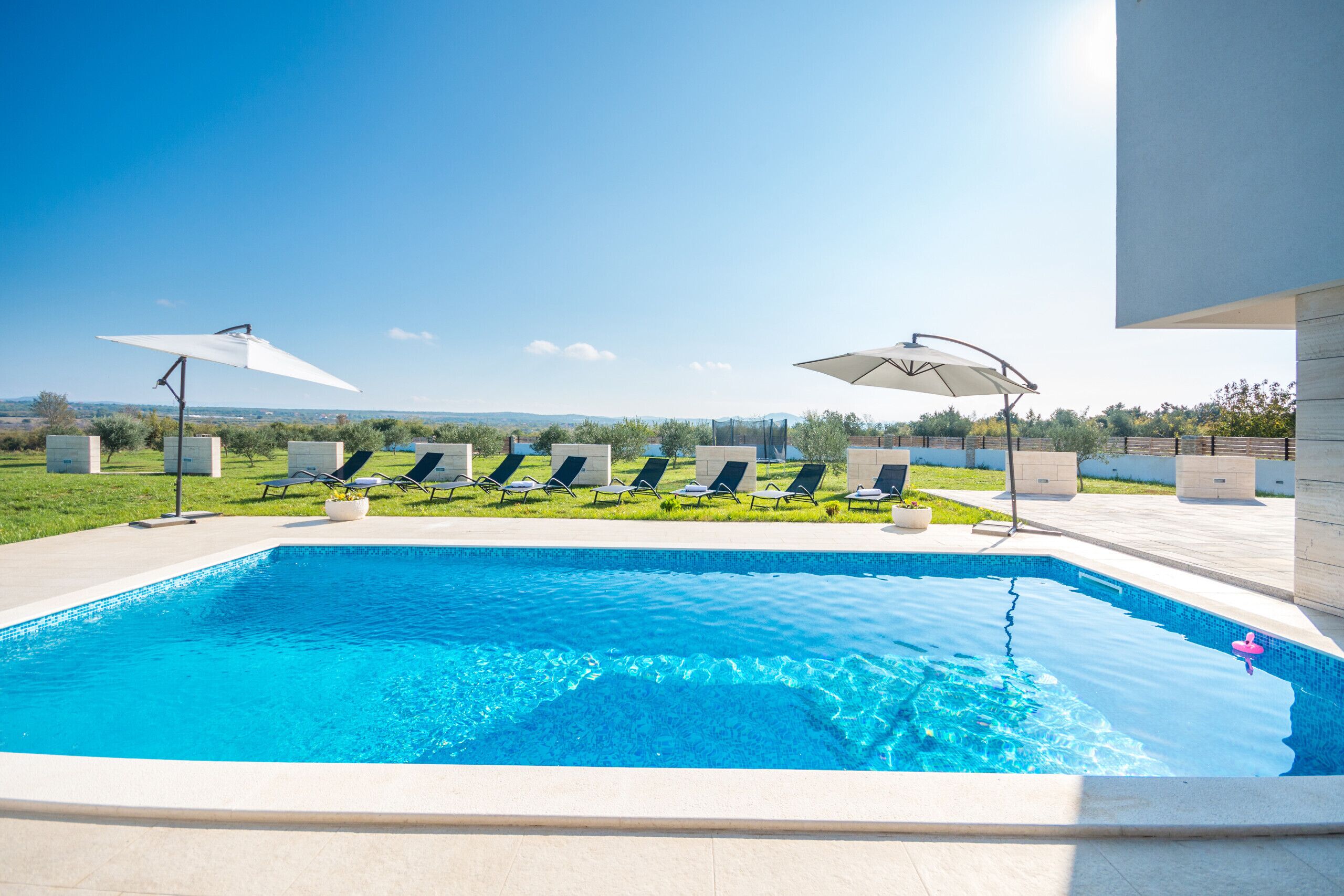 A swimming pool with lounge chairs and umbrellas, surrounded by a landscaped garden and a clear view of the mountains.